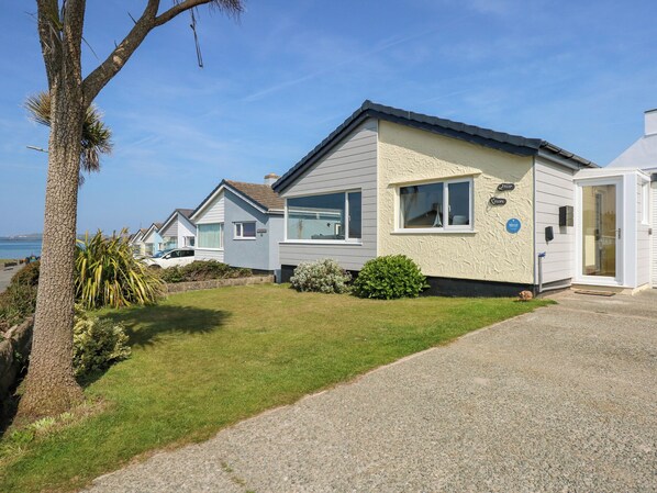 A row of mobile homes with a grassy lawn and a tree, near a body of water. - Flip Flops (Rhosneigr)