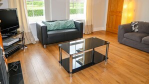 Una sala de estar con un sofá de cuero negro, un sofá gris, una mesa de centro de vidrio y un televisor sobre un mueble.