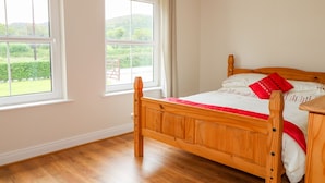 Una cama de madera en una habitación con dos ventanas, paredes blancas y vistas al verdor exterior.
