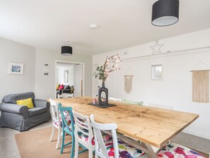 A modern living room with a wooden dining table, white chairs, a grey sofa, and a macrame wall hanging. - Gorwel (Moelfre)