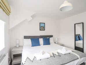 A modern bedroom with a large bed, a bedside table with a lamp, a mirror, and a framed picture on the wall. - Gorwel (Moelfre)