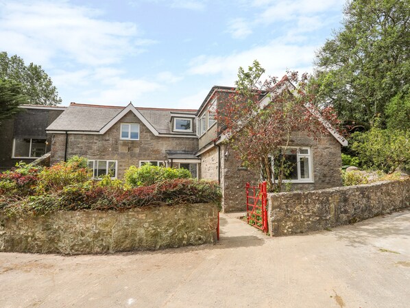 A stone house with a red gate, surrounded by greenery and a clear sky. - Gorwel (Moelfre)