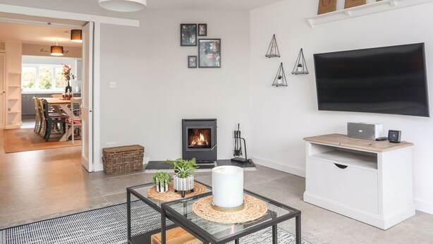 Ein modernes Wohnzimmer mit Kamin, Flachbildfernseher und Essbereich, der durch eine offene Tür einsehbar ist.