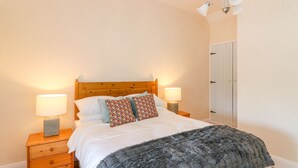 A bedroom with a wooden headboard, two bedside tables with lamps, a grey blanket, and patterned pillows. - The Lodge at Raheengraney House (Raheengraney)