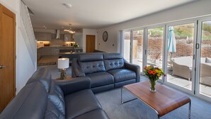 A modern living room with a sectional sofa, a coffee table, and a view of the kitchen and outdoor patio.