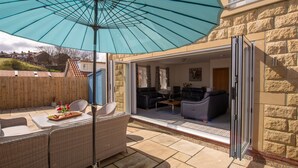 An outdoor patio with a large umbrella, wicker furniture, and a view of the interior through an open door.