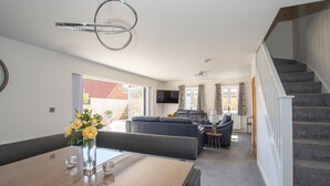 A spacious living area with a dining table, sofas, and a staircase.