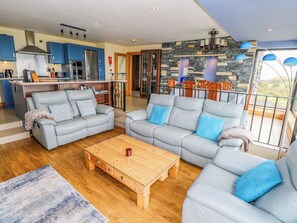 A modern living room with two grey sofas, a wooden coffee table, and a kitchen in the background. - Ocean Sail House (Maghery)
