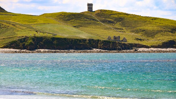 A coastal landscape with a grassy hill, a stone tower, and a ruined structure. - Ocean Sail House (Maghery)