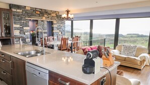 A modern kitchen with a stone backsplash, a built-in dishwasher, and a large island with a coffee maker. - Ocean Sail House (Maghery)