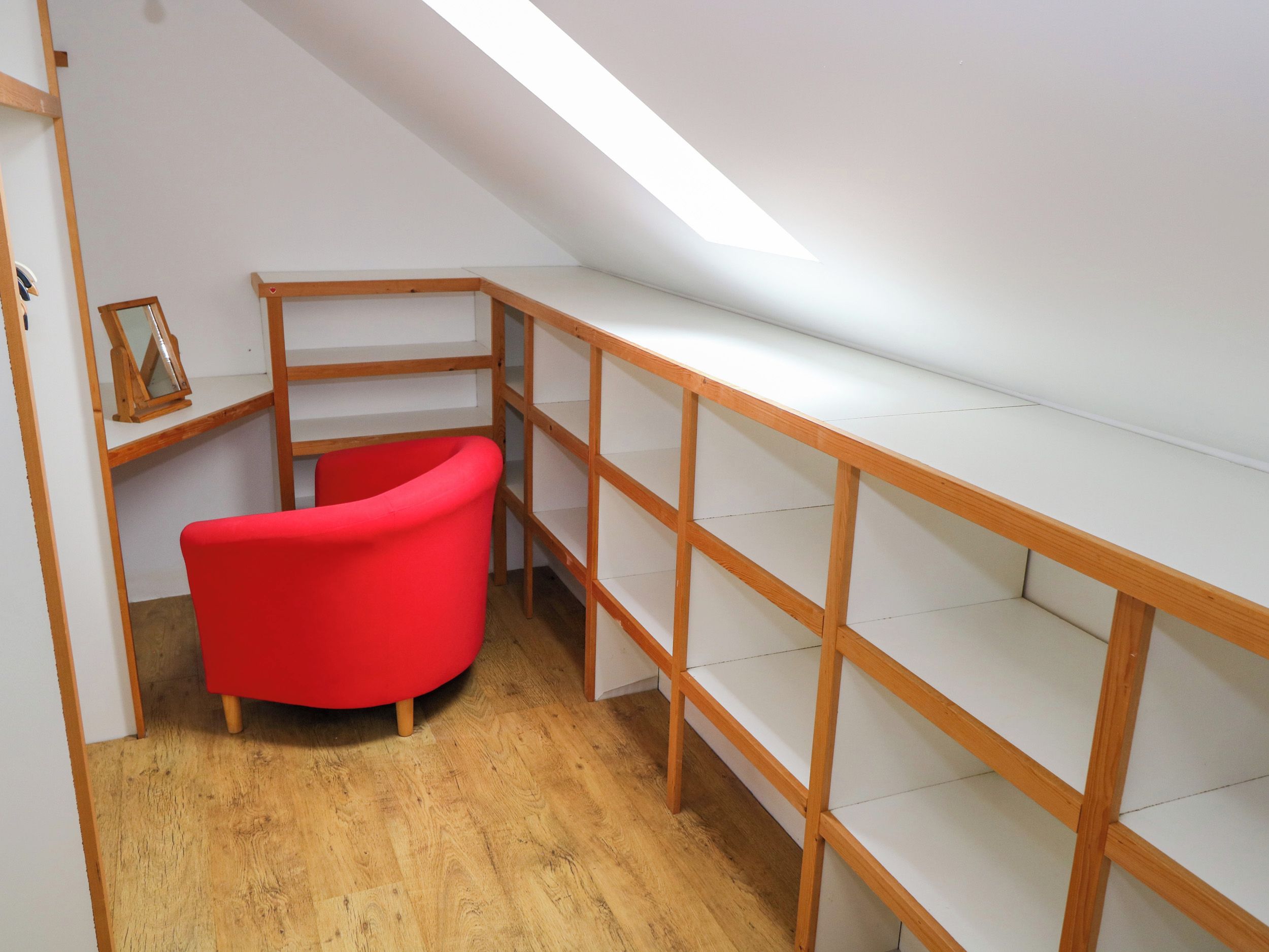 Una habitación con una silla roja, estanterías de madera y techo inclinado.