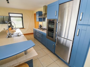 A modern kitchen with blue cabinets, stainless steel appliances, and a built-in oven. - Ocean Sail House (Maghery)