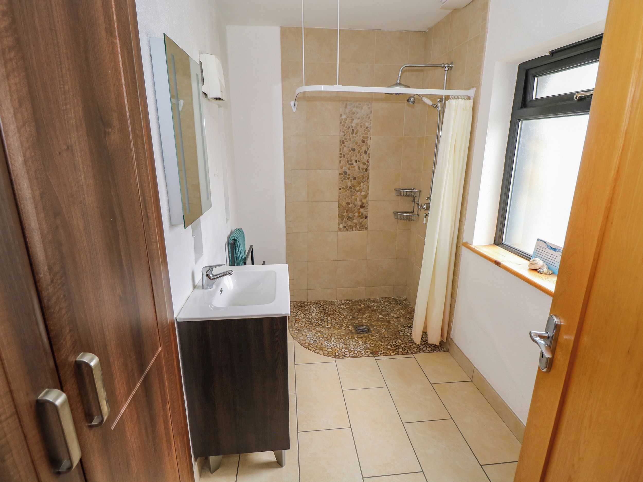 A bathroom with a shower, a sink, and a window.