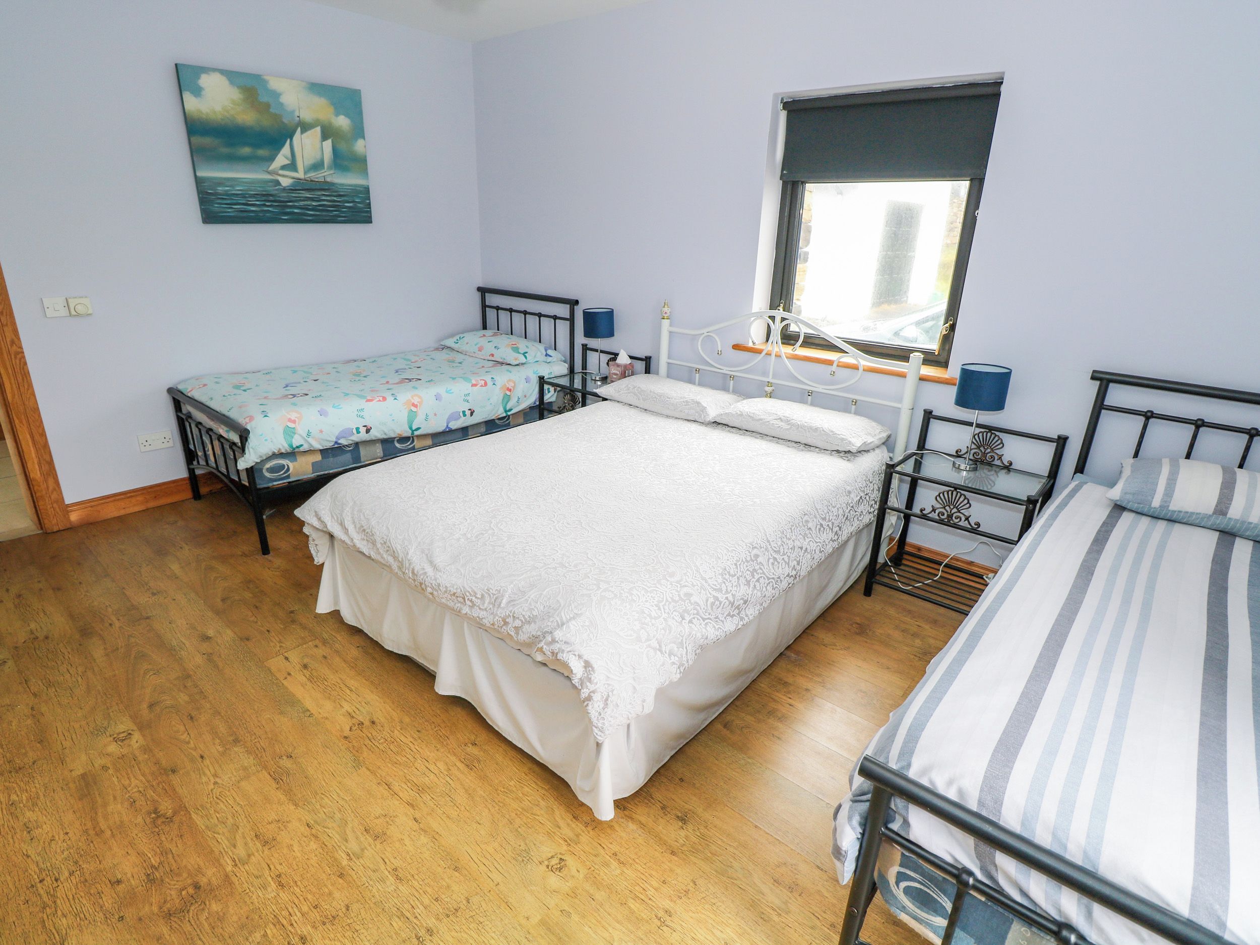 Ein Schlafzimmer mit einem großen Bett, zwei kleineren Betten, einem Fenster und einem Bild an der Wand.