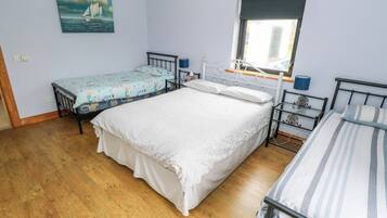Ein Schlafzimmer mit einem großen Bett, zwei kleineren Betten, einem Fenster und einem Bild an der Wand.