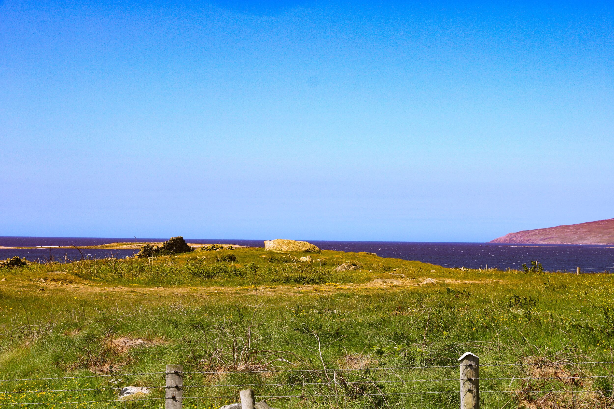 Eine Küstenlandschaft mit einer Wiese, einem Holzzaun und einer großen Felsformation.