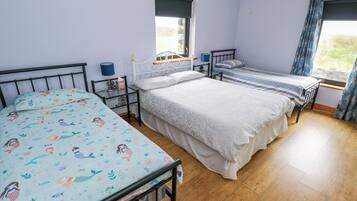 A bedroom with two single beds, a window with curtains, a bedside table with a lamp, and a wall-mounted shelf.
