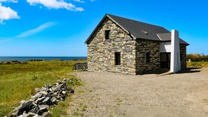 A stone building with a sloped roof, a small window, and a door. - Ocean Sail House (Maghery)