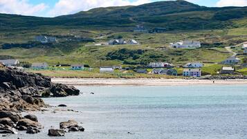 A coastal village with houses on a hillside, a rocky shoreline, and a clear view of the sea.