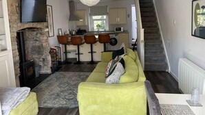 Un salon moderne avec une cheminée en pierre, un canapé, une table basse et un coin cuisine équipé d’un four à micro-ondes et d’un lave-linge.