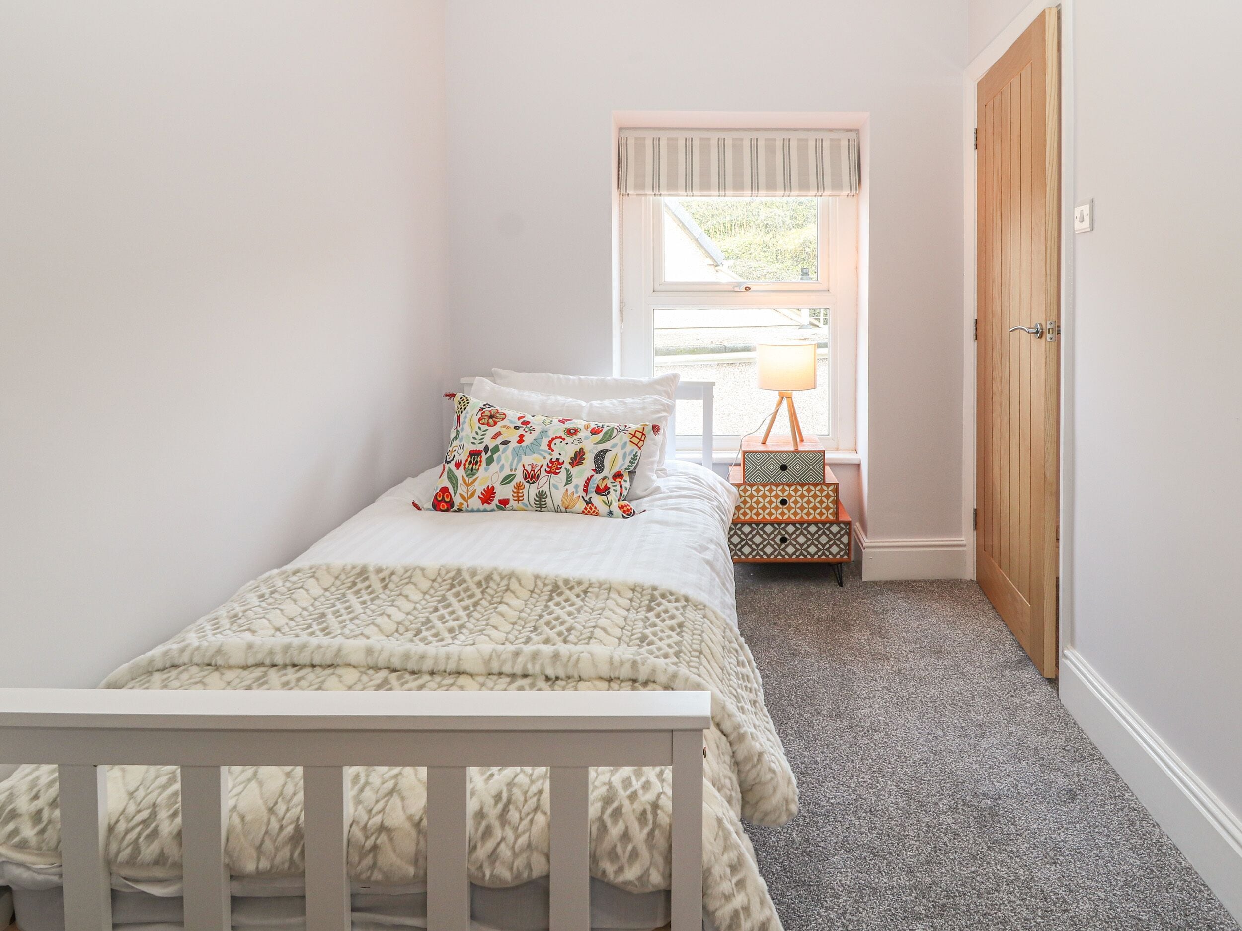 A bedroom with a bed, a nightstand, a lamp, a window, and a door.