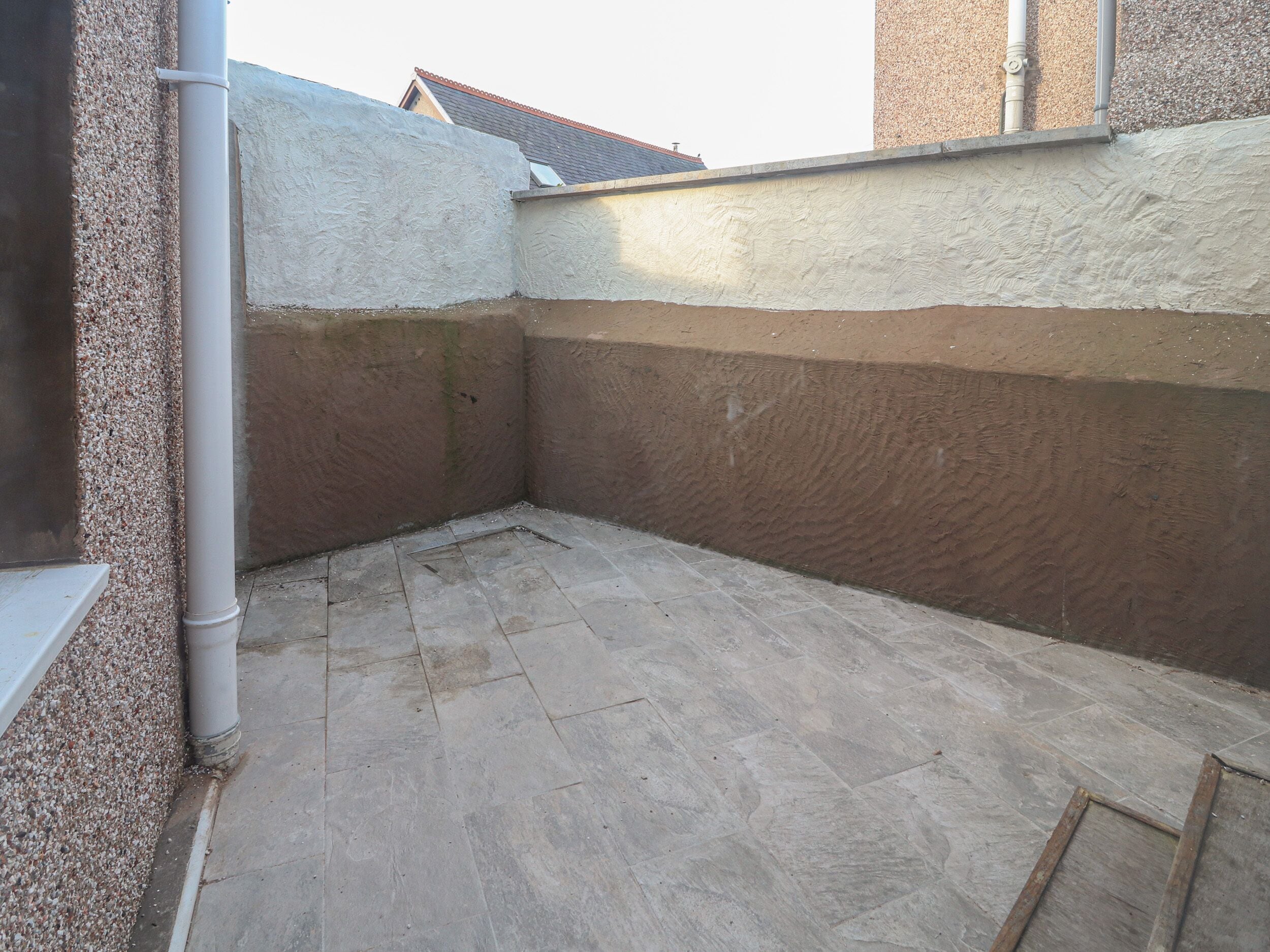 A corner of a building with a tiled floor, a white pipe, and a textured wall.
