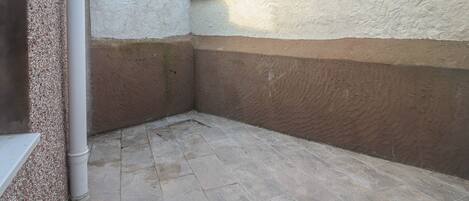 A corner of a building with a tiled floor, a white pipe, and a textured wall.