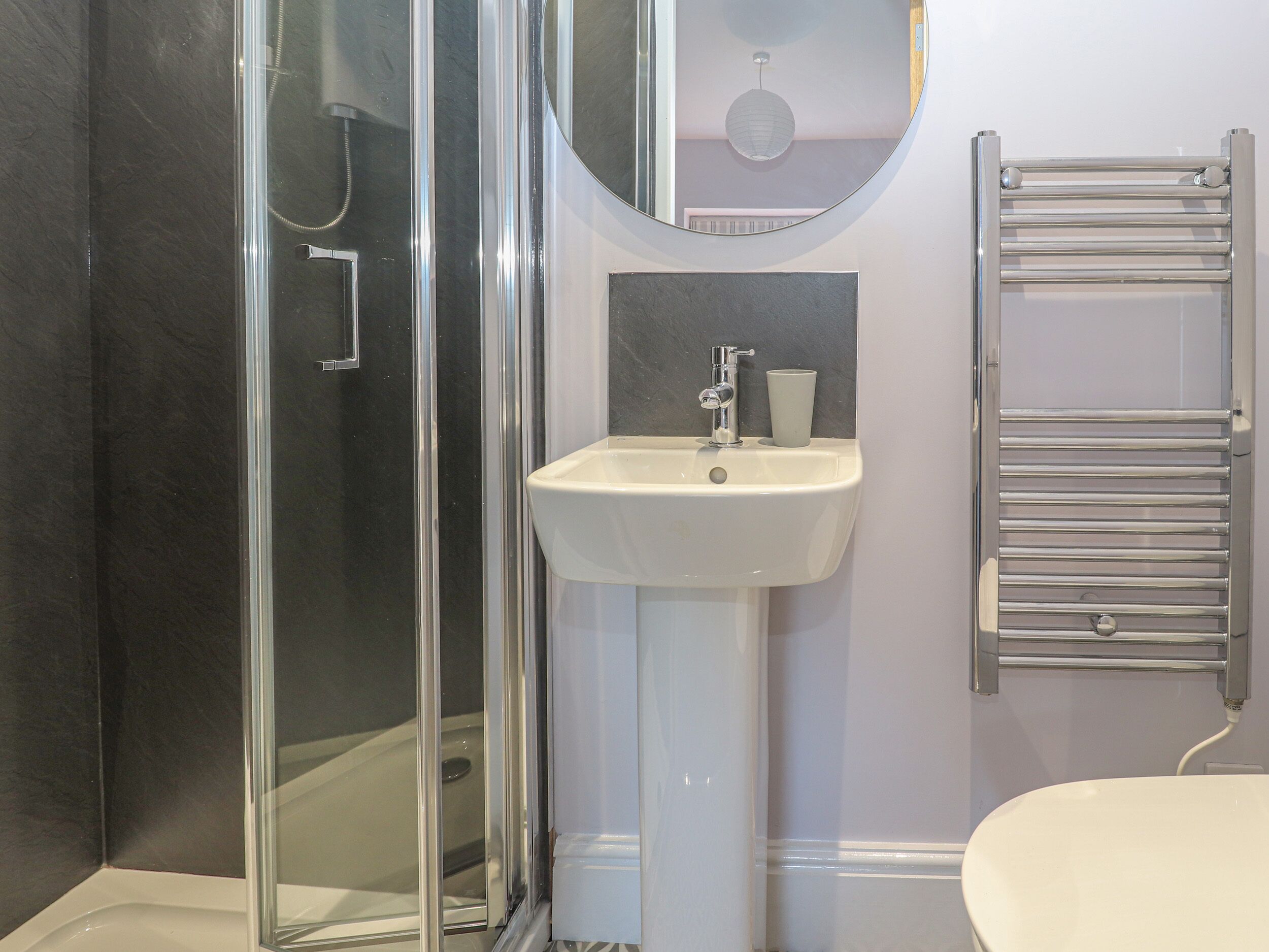 A bathroom with a glass shower enclosure, a white sink with a mirror above it, and a towel rack.