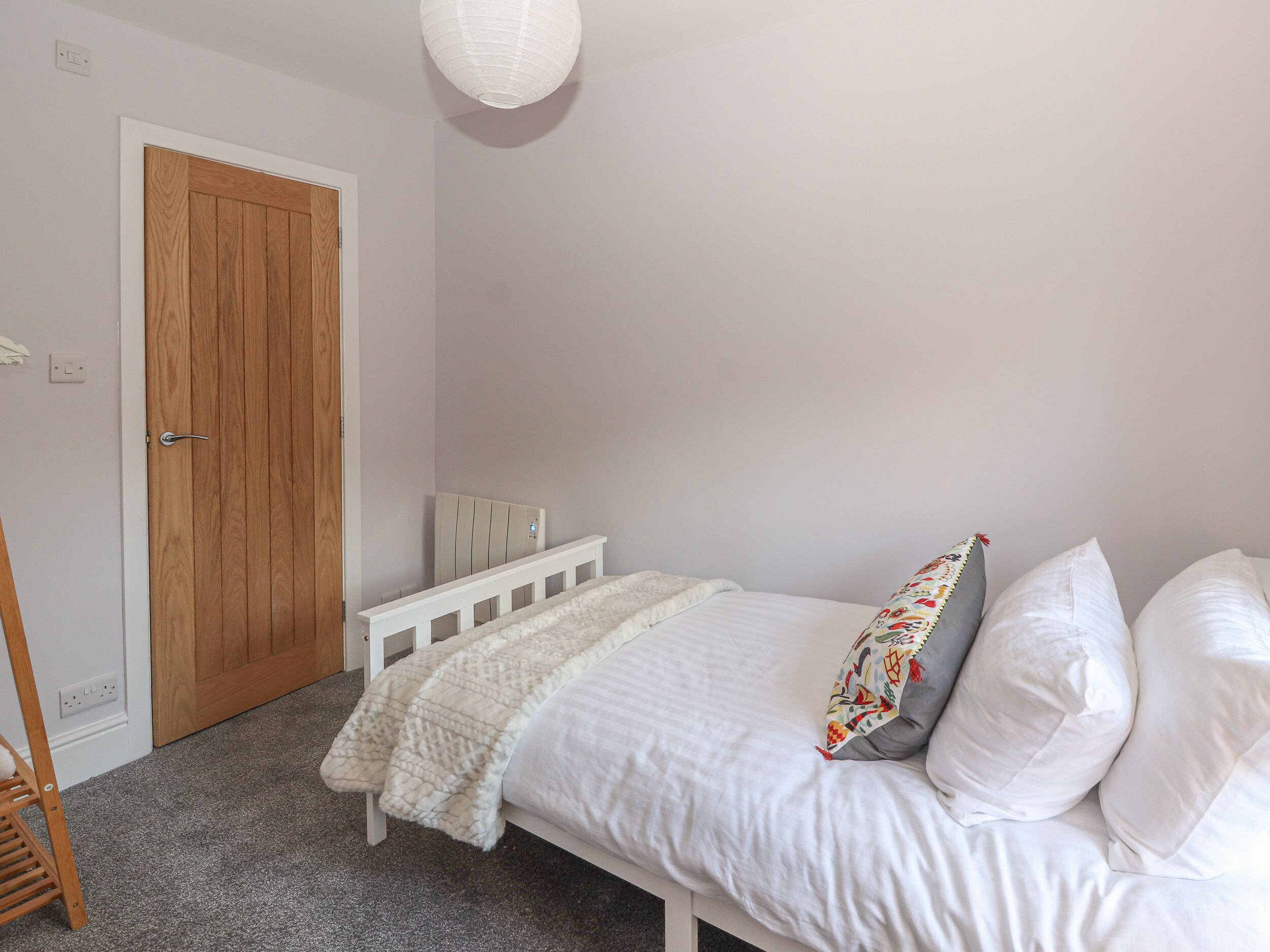 Een slaapkamer met een wit bed, een houten deur en een witte radiator.