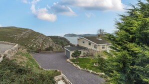 Una casa con camino pavimentado, muro de piedra y vistas a un lago y colinas.