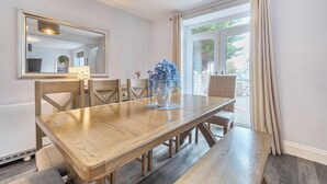 Un comedor con una mesa de madera, sillas, un jarrón de flores, un espejo y vistas al exterior a través de un ventanal.