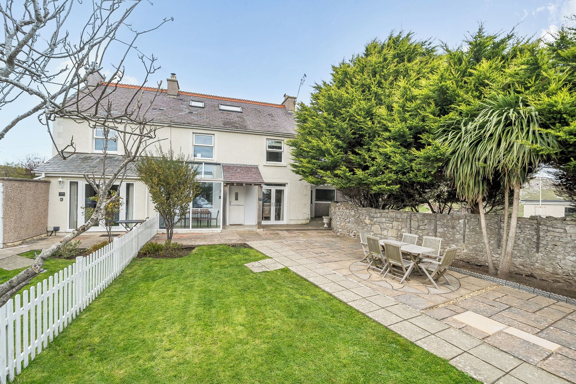 A two-story house with a stone wall, a grassy backyard, and a patio with outdoor furniture.