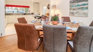 A dining area with a table set for six, surrounded by six chairs. There is a potted plant on the table, and a painting on the wall. - Casalmare (Exmouth)