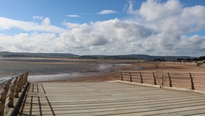A wooden boardwalk leading to a beach with a clear sky and distant hills. - Casalmare (Exmouth)
