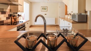 Uma cozinha moderna com uma pia de aço inoxidável, bancadas de madeira, forno embutido e micro-ondas.