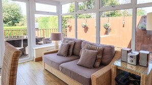 Um quarto aconchegante com um sofá de vime, uma mesa de vidro e vista para um jardim através de grandes janelas.