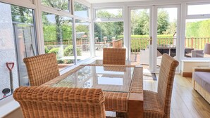 Uma sala de jantar com cadeiras de vime e uma mesa de vidro, grandes janelas e vista para o jardim.
