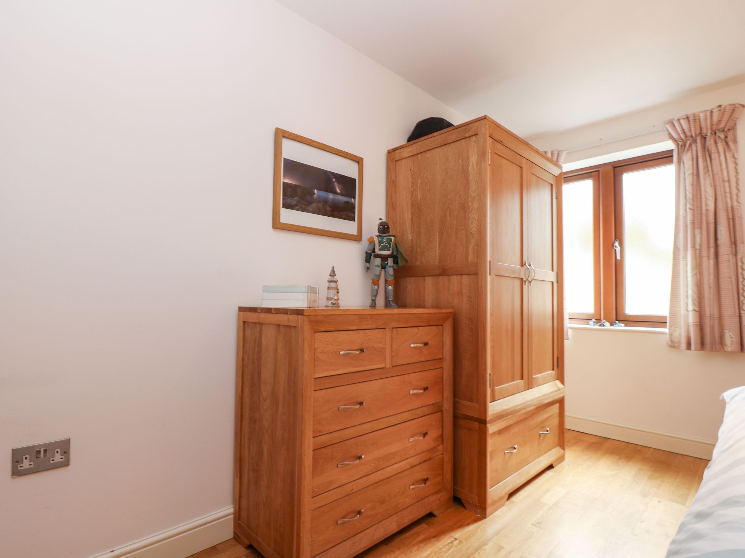 Une chambre à coucher avec une armoire en bois, une table de chevet, une fenêtre avec des rideaux et un tableau encadré au mur.