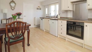 A modern kitchen with white cabinetry, a built-in oven, and a dining area with a wooden table and chairs. - Cartwheel Cottage (York)