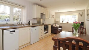 A kitchen with white cabinets, a dishwasher, and a dining area with a wooden table and chairs. - Cartwheel Cottage (York)