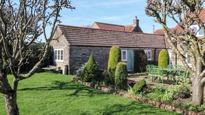 A stone house with a tiled roof, a well-maintained lawn, and a garden with various plants. - Cartwheel Cottage (York)