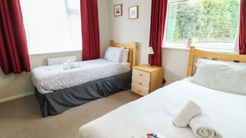 A hotel room with two beds, a nightstand, a lamp, and a window with curtains.