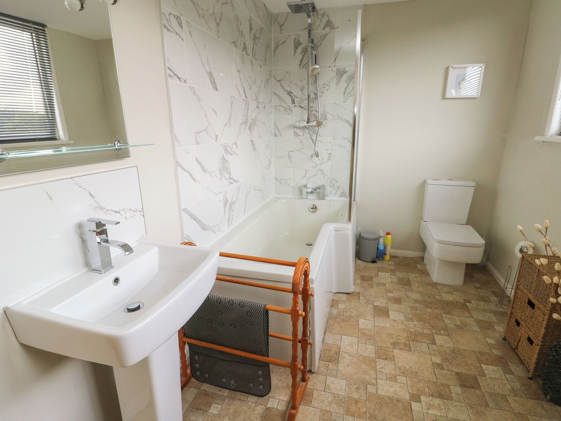 A bathroom with a marble shower, a white sink, and a toilet.