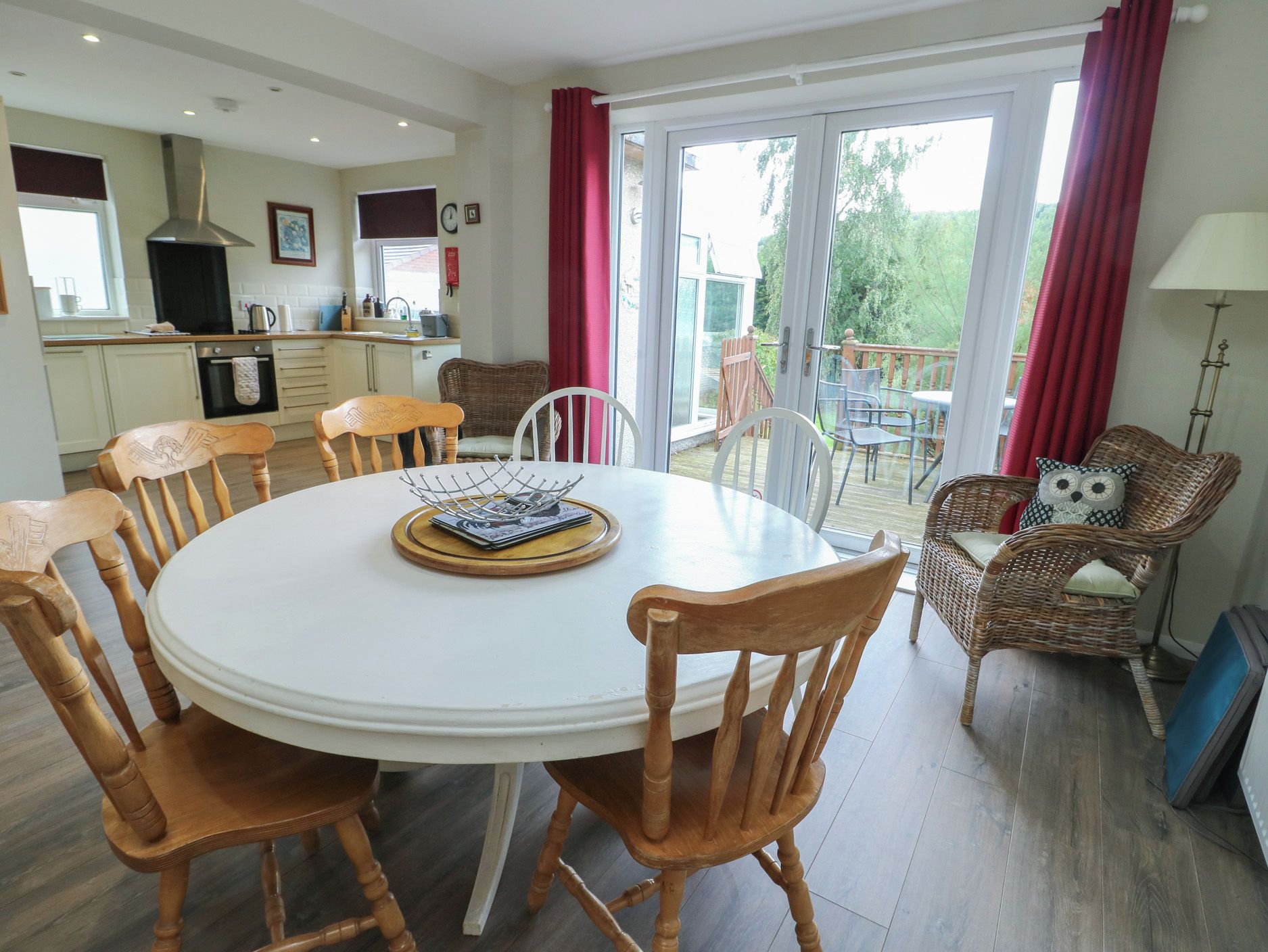 A dining area with a round table, wooden chairs, and a view of the garden through glass doors.