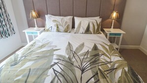 A neatly made bed with a leaf-patterned bedspread, two bedside tables with lamps, and a headboard. - May Cottage (Scarborough)