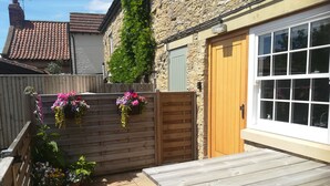 A wooden bench and a table in a courtyard with a stone wall, a wooden gate, and hanging flower baskets. - May Cottage (Scarborough)