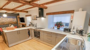 A modern kitchen with wooden beams, stainless steel appliances, and a large window with a flower vase. - May Cottage (Scarborough)