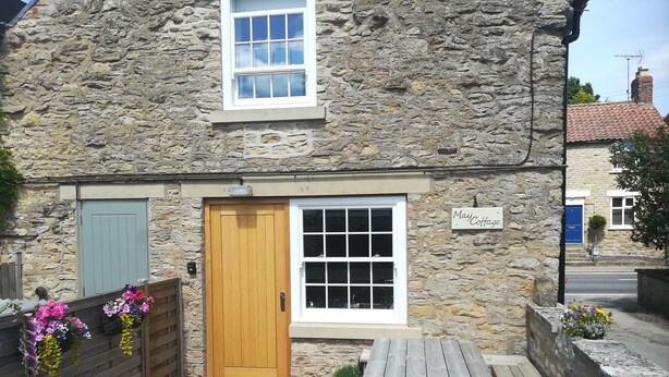 A stone cottage with a wooden door, a small window, and a sign reading "May Cottage". - May Cottage (Scarborough)
