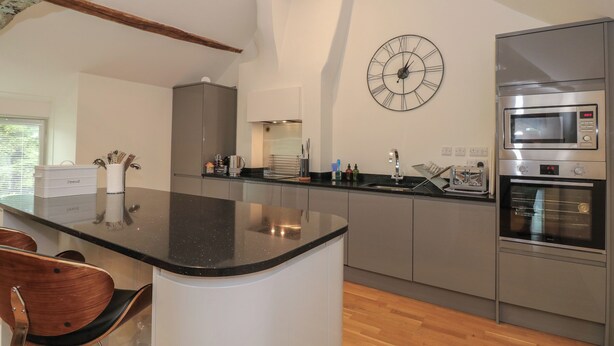 Een moderne keuken met een centraal eiland, roestvrijstalen apparatuur en een grote wandklok.