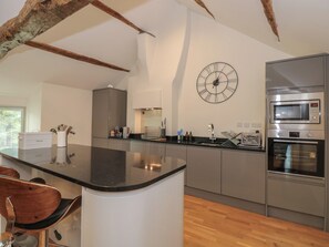 A modern kitchen with a central island, stainless steel appliances, and a large wall clock. - Low Melbecks House (Keswick)